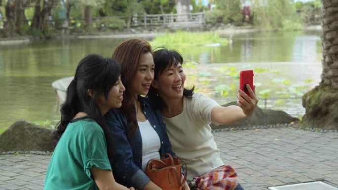 三名亚洲女性在崇山公园的湖边拥抱和自拍