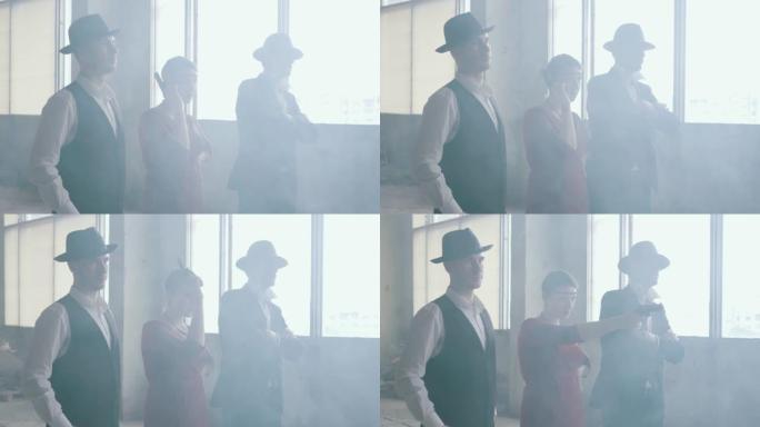 三个匪徒，两个男人戴软呢帽，穿着古典西装，一个女人穿着时髦的衣服站在烟雾中