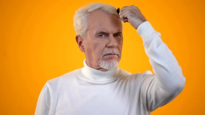 男性养老金领取者梳理白发，震惊地看着发刷，trichology