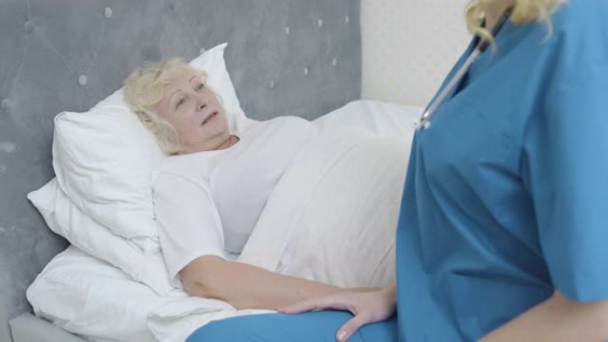 生病的老妇人躺在床上与年轻的医生交谈，在家中提供医疗服务
