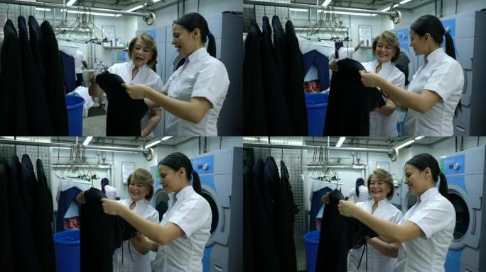 友好的年轻女子在工业洗衣店训练一个成熟的女人，解释衣架上的衣服
