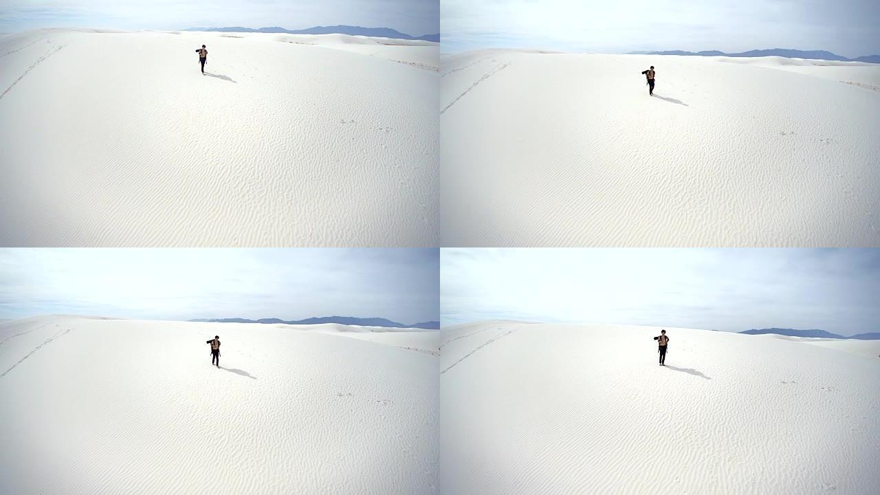 年轻的纹身高加索人，带着大背包的游客，从沙丘上走下来的沙质沙漠。美国新墨西哥州白沙国家纪念碑。空中无