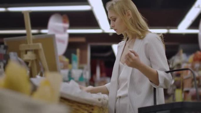 迷人的女孩顾客正在面包店购物，闻起来，微笑着，放进购物车。健康生活方式和超市理念
