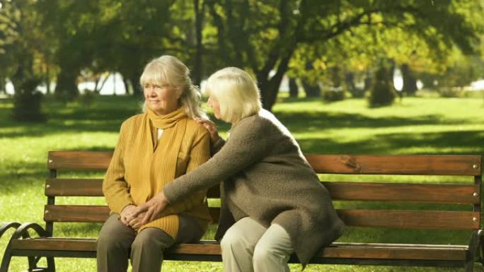 资深女士坐在公园的长凳上安慰老朋友的损失