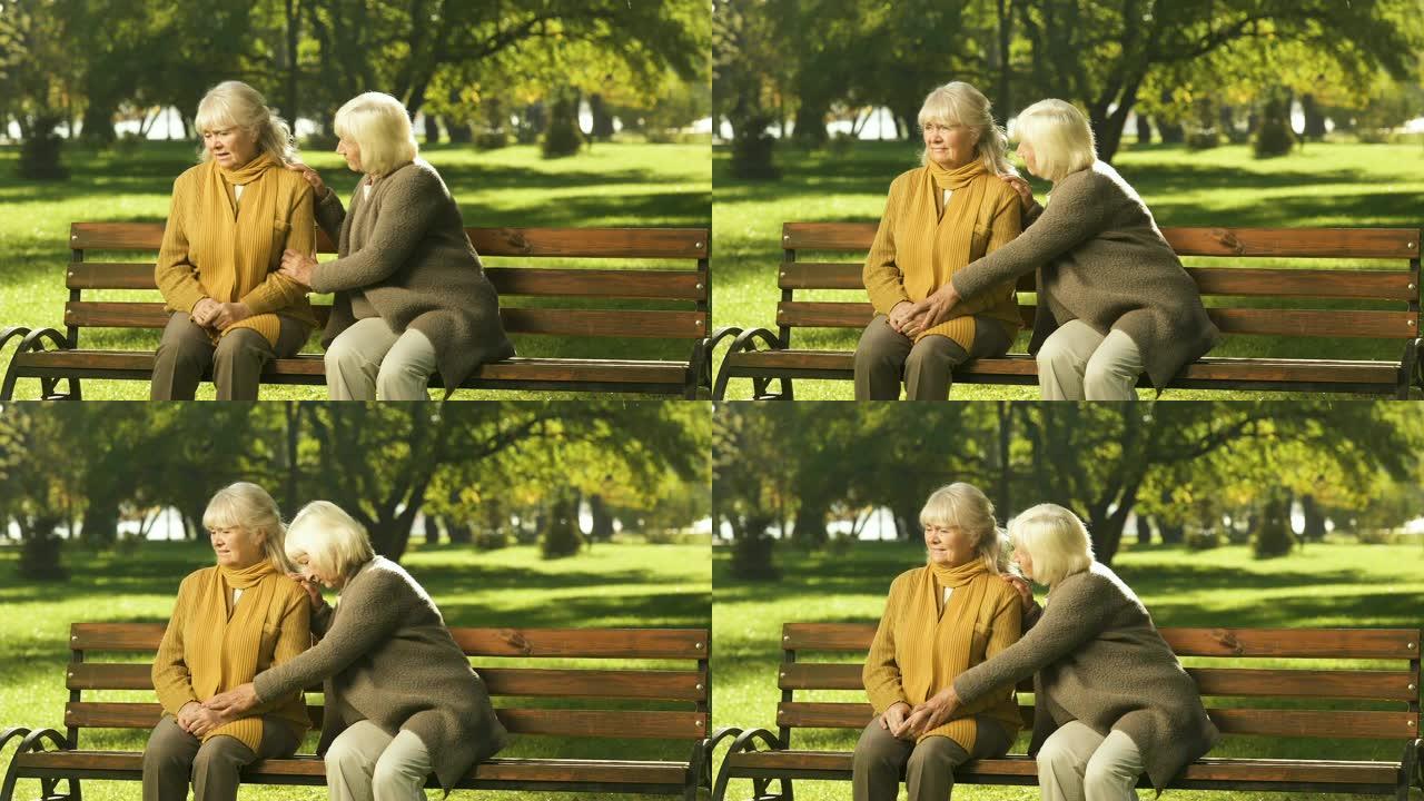 资深女士坐在公园的长凳上安慰老朋友的损失