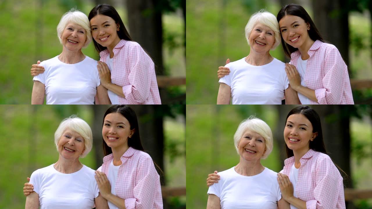 年轻女子和年迈的祖母在镜头前微笑，在户外放松