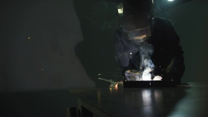 火花飞舞时，一个人在车间的金属焊接台上焊接MIG