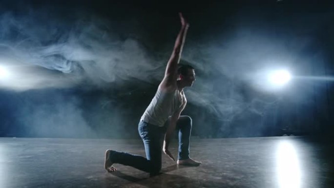男舞者在聚光灯下的烟雾中表演了一个特技跳跃，并在场景中旋转了一圈。现代芭蕾。