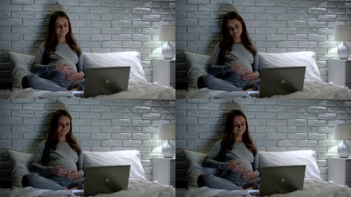 快乐孕妇抚摸肚子，在互联网上观看教育视频