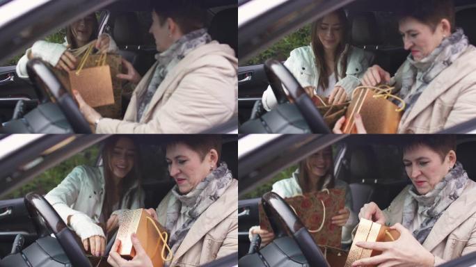 年轻的高加索女孩在汽车沙龙里给年长的女人送礼品袋。女儿与母亲见面并赠送礼物。一家人一起开车。