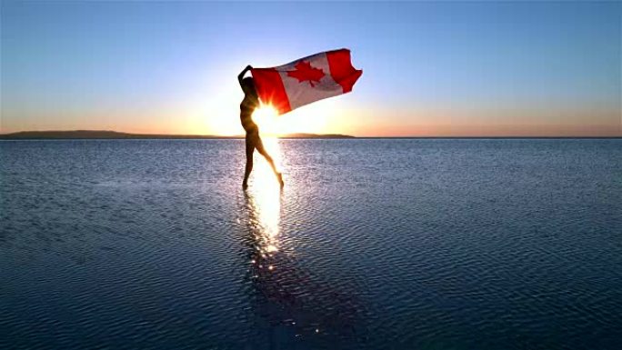 美丽的芭蕾舞演员在水上举着加拿大国旗。有风的一天。慢动作