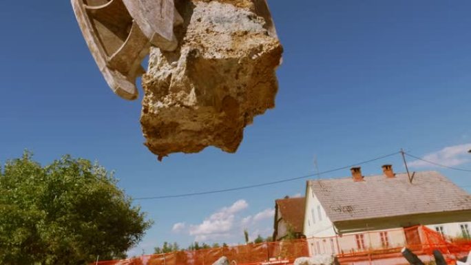 挖掘机抓斗在阳光下压碎一堆建筑垃圾上方的一块混凝土