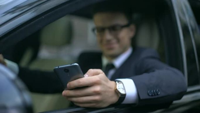 穿着商务服装的男人在智能手机上发短信，坐在汽车上微笑