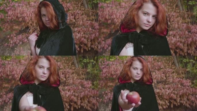 穿着黑色礼服的神秘红发高加索女孩转向镜头，提议红苹果。