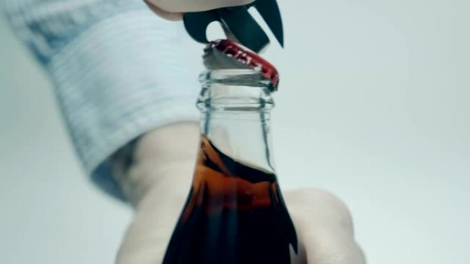一个有开瓶器的男人用冷却饮料在玻璃瓶中打开金属软木塞