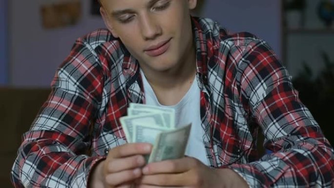 帅气少年数着美元钞票，坐在桌旁，做梦购买