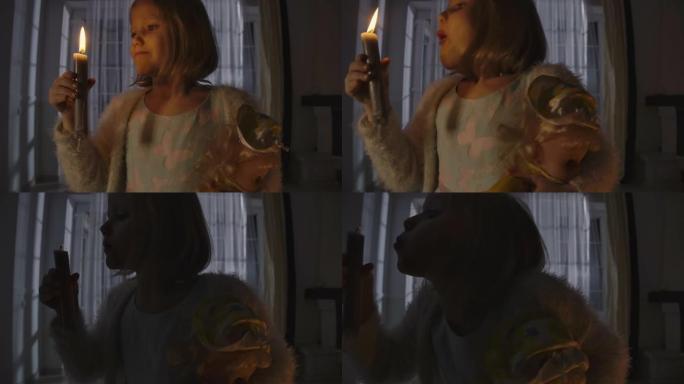奇怪的高加索女孩吹蜡烛，另一只手拿着洋娃娃的特写肖像。奇怪的孩子晚上独自一人。恐惧，恐惧，奇怪。