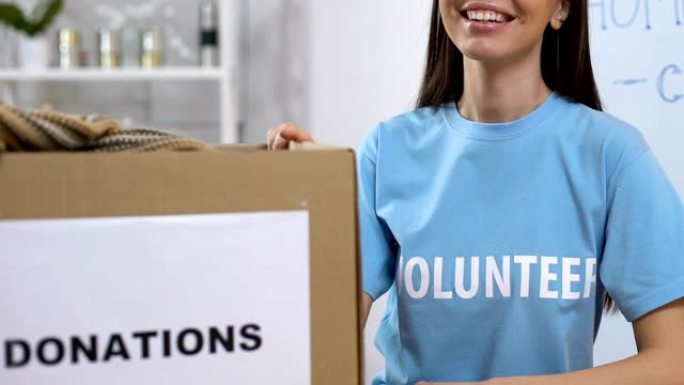 微笑的志愿者站在箱子旁，带着捐赠的衣服，无家可归的援助