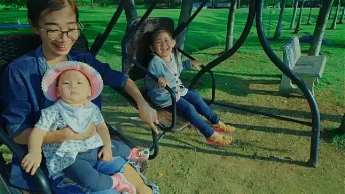 年轻的母亲和两个女儿在公园的秋千椅上休息和享受大自然