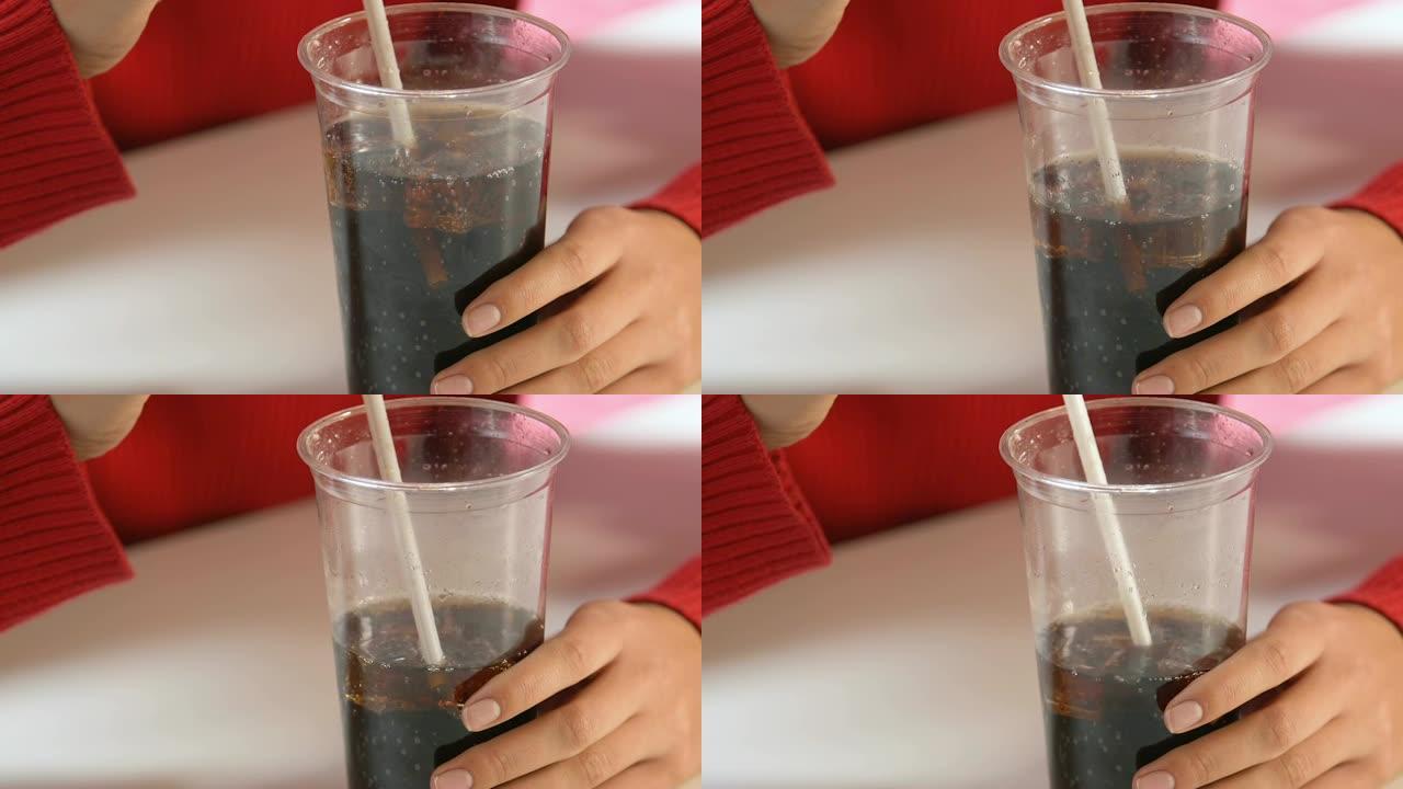 女性双手拿着苏打水的塑料玻璃，不健康的含糖饮料，特写