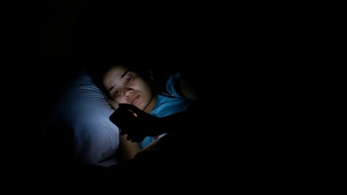晚上在床上使用智能手机的亚洲妇女