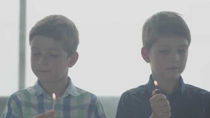 两个双胞胎兄弟在窗前的烟雾弥漫的房间里玩火。