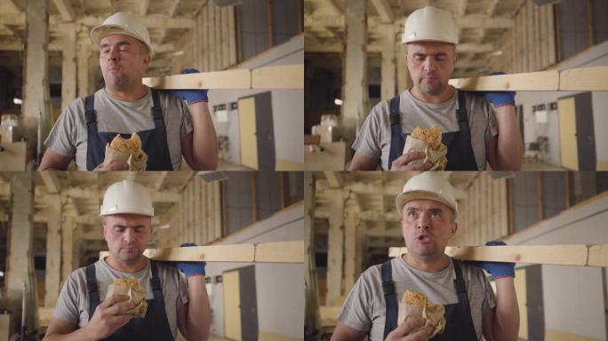一个肌肉发达的高加索建筑工人的肖像，棕色的眼睛在建筑工地吃面包。强壮的年轻工人在工作中吃午饭。戴着白