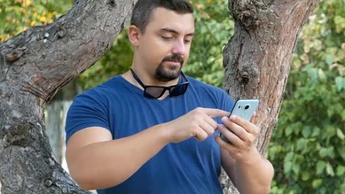 那家伙站在公园的一棵树旁，用他的智能手机