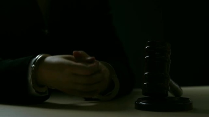 戴着手铐的法官把手放在书桌旁的木槌上，贪污，贿赂