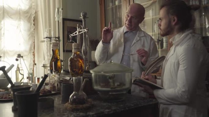 两个白种人站在桌子旁，他们带着古老的烧瓶，试管和化学设备。年长的药剂师教年轻的同事。复古药房，复古药
