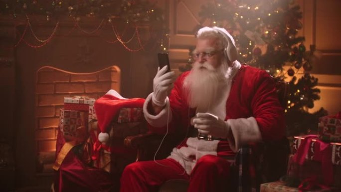 手里拿着耳机和手机跳舞的圣诞老人。在线听音乐。生涩而动感的歌曲