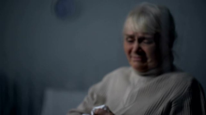 沮丧的老年妇女在雨天在黑暗的房间里深深地哭泣，孤独