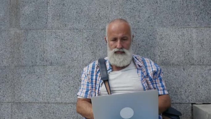大胡子的老人带着笔记本电脑在城市快乐地微笑