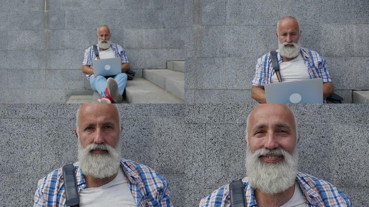 大胡子的老人带着笔记本电脑在城市快乐地微笑