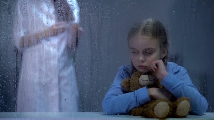 护士给生病的小女孩注射，在下雨的窗户后面拥抱泰迪熊