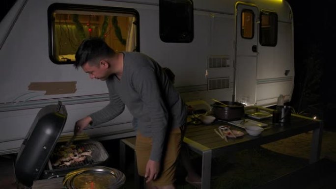 情侣们在晚上做烧烤烧烤晚餐，在休闲车里自然旅行，在家里开车回家的露营车。