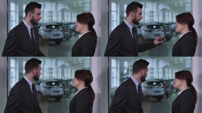 严肃的高加索男人和女人站在汽车经销店聊天的侧视图。男性经销商向女性客户解释汽车规格。电影院4k Pr