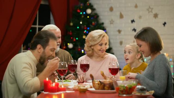 可爱的小女孩在圣诞晚宴上与家人讲故事，每个人都微笑着