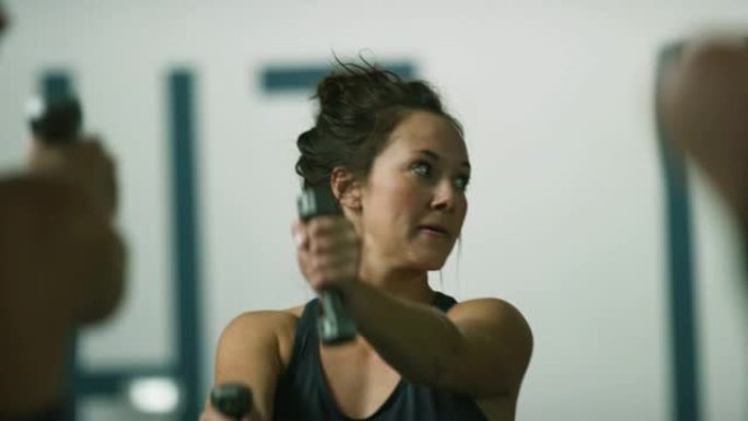 一位二十多岁的迷人白人妇女在健身工作室的课堂上用手的重量进行肩部锻炼