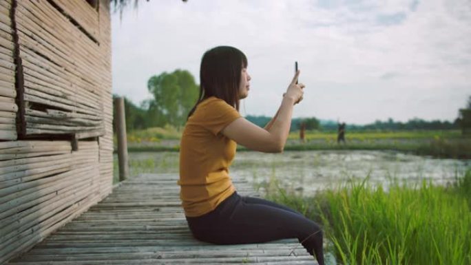 迷人的女性在稻田用智能手机拍照