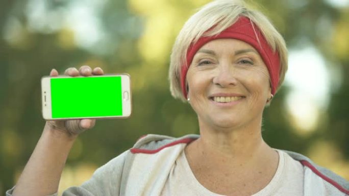 微笑健美中年女子秀绿屏手机，运动app
