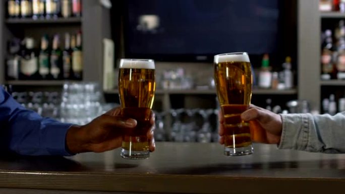两名男子在酒吧的酒吧柜台碰碰啤酒杯，下班后放松