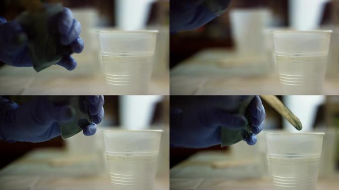一个戴着安全手套的人使用木制工艺棒将粉状颜料铲入透明环氧树脂/树脂的小塑料杯中