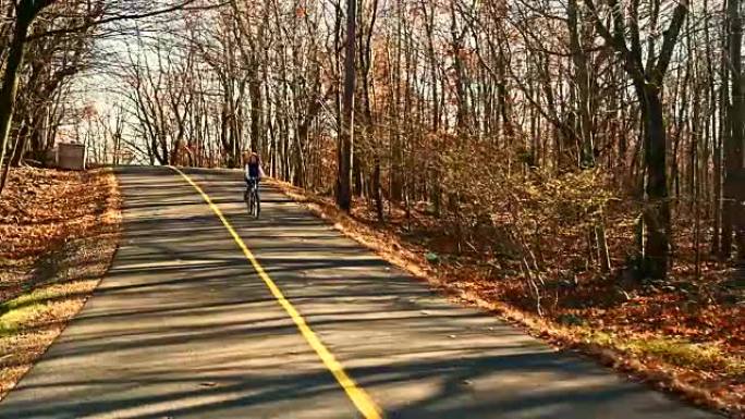 十几岁的女孩在秋天的森林里骑自行车在路上
