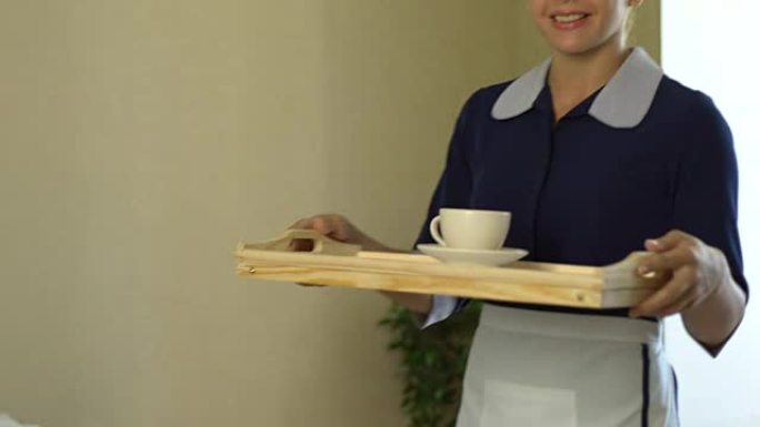 微笑的女仆将客户咖啡放在托盘上，五星级酒店的服务无可挑剔