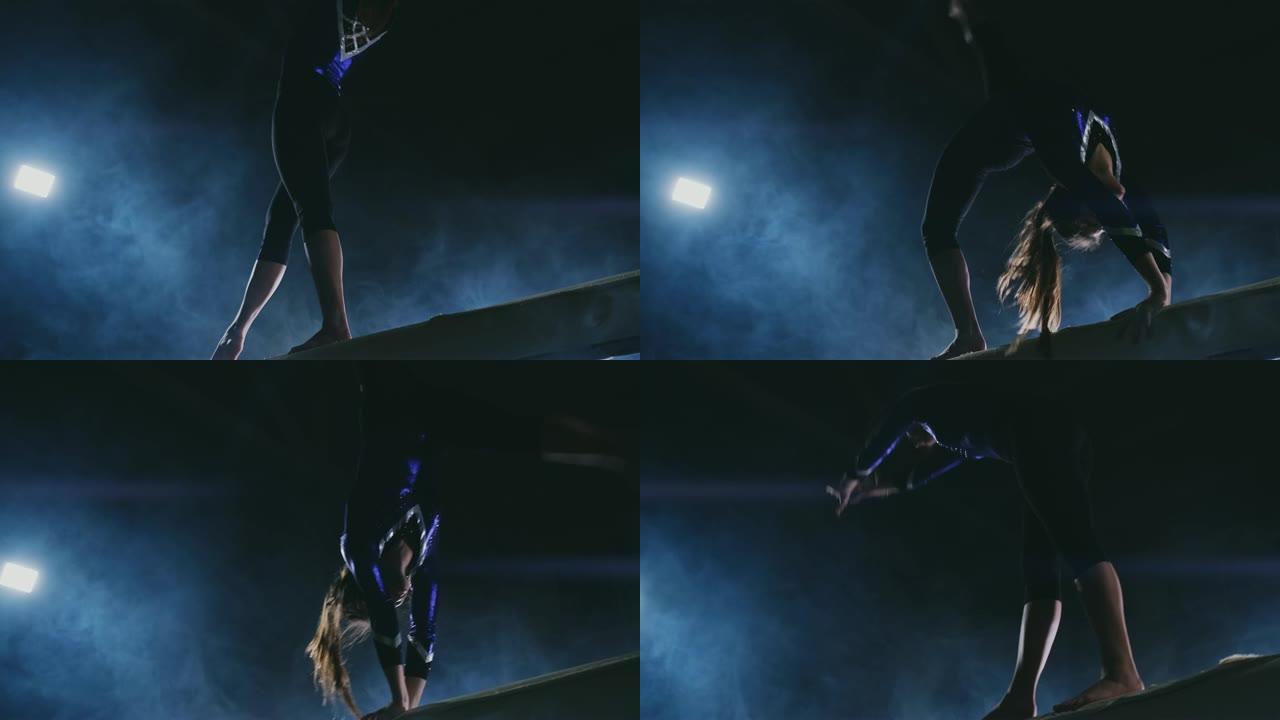 女子艺术体操。在烟雾中慢动作，女孩在平衡木上表演奥林匹克计划的复杂元素