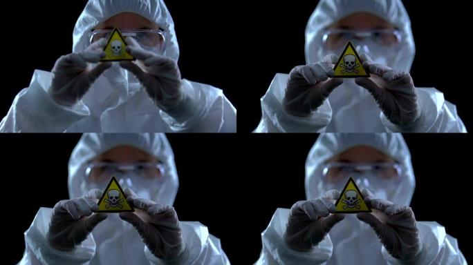 穿着防护长袍的女性向相机展示毒物标志，生命威胁