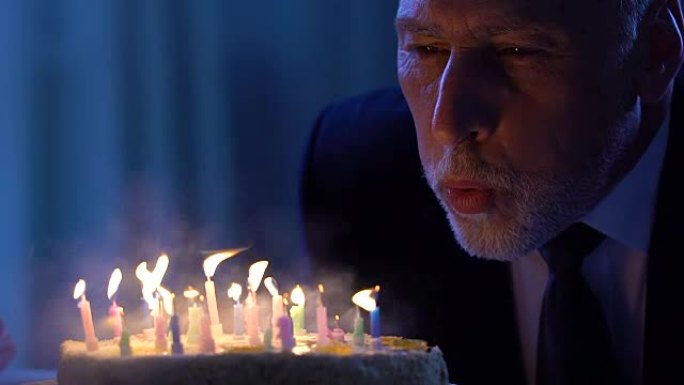 开朗的老人吹着蛋糕蜡烛庆祝生日，幸福
