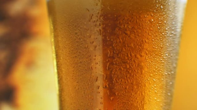 在带有橙色液体的玻璃杯中升起的细气泡的宏观镜头。装有水滴的玻璃杯中的冷淡啤酒。精酿啤酒特写。旋转36