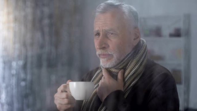 穿着围巾的老人患有喉咙痛，在家喝热茶，健康
